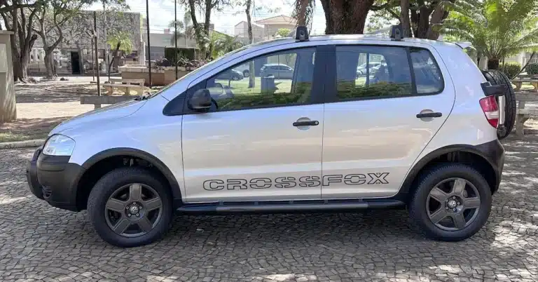 SUV Volkswagen CrossFox prateado estacionado em uma rua de paralelepípedos, com estepe fixado na parte traseira e rack de teto visível na vista lateral.