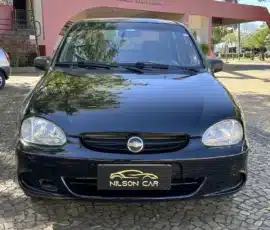 Vista frontal de um carro Chevrolet preto estacionado em uma entrada de paralelepípedos; uma placa de concessionária com a inscrição "Nilson Car" é visível em primeiro plano.