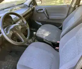 Interior de um carro compacto: volante à esquerda, bancos de tecido cinza e alavanca de câmbio manual entre os bancos.