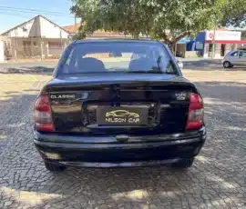 Vista traseira de um sedã preto estacionado em um pátio de paralelepípedos; são visíveis as lanternas traseiras, o vidro traseiro e uma placa "Nilson Car" (emblema "Classic" à esquerda).
