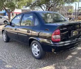 Sedã preto de quatro portas estacionado em uma rua de paralelepípedos com árvores acima, dia ensolarado.