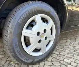 Close-up de um pneu de carro e uma calota prateada da Chevrolet em um veículo preto, estacionado em uma entrada de paralelepípedos.
