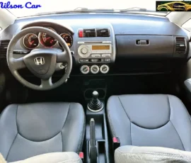 Interior view of a compact car showing the steering wheel, central dashboard with radio and climate controls, and a manual gear shift between two grey front seats. Watermarks read 'Nilson Car' and a small graphic logo are visible.