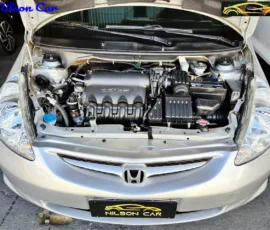 Front view of a silver Honda with the hood open, exposing the engine bay and components like battery and air intake; Nilson Car branding is visible on the license plate and top corner.