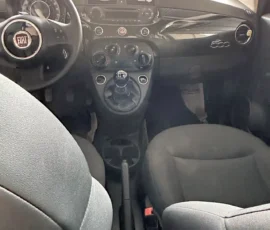 Interior view of a Fiat 500: steering wheel with Fiat emblem, center console and manual gear shift visible under the dash.