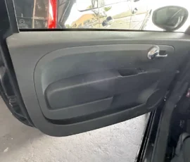 Interior of a car door panel: gray molded armrest with a chrome door handle and small window control area.