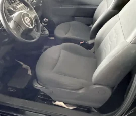 Interior of a compact car showing the steering wheel, manual gear shift, and two front seats with dark upholstery