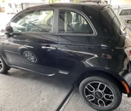 Black Fiat 500 parked in a dealership lot, showing the driver’s side and rear quarter panel.