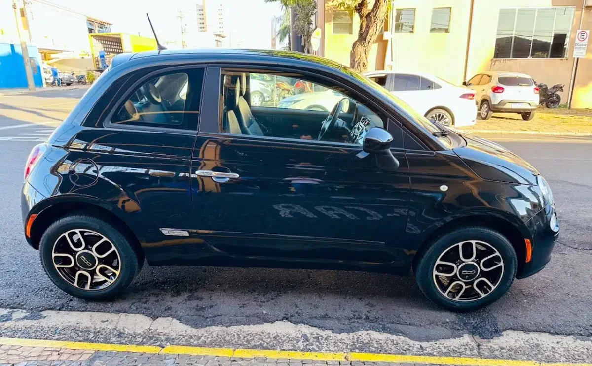 Black compact two-door car parked on a city street, side view showing alloy wheels and chrome door handles