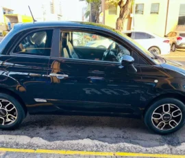 Black compact two-door car parked on a city street, side view showing alloy wheels and chrome door handles