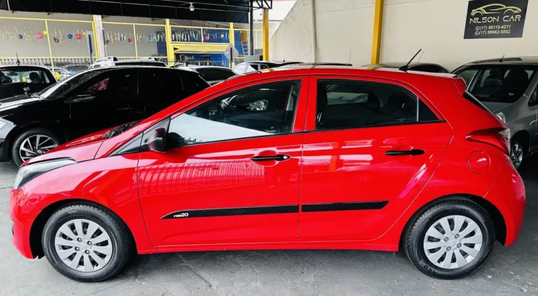 Red Hyundai HB20 hatchback parked at a car dealership lot with other vehicles in the background
