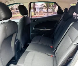 Rear seating area of a car with gray fabric seats and headrests, seen from the open door with a park and parked cars outside the window.