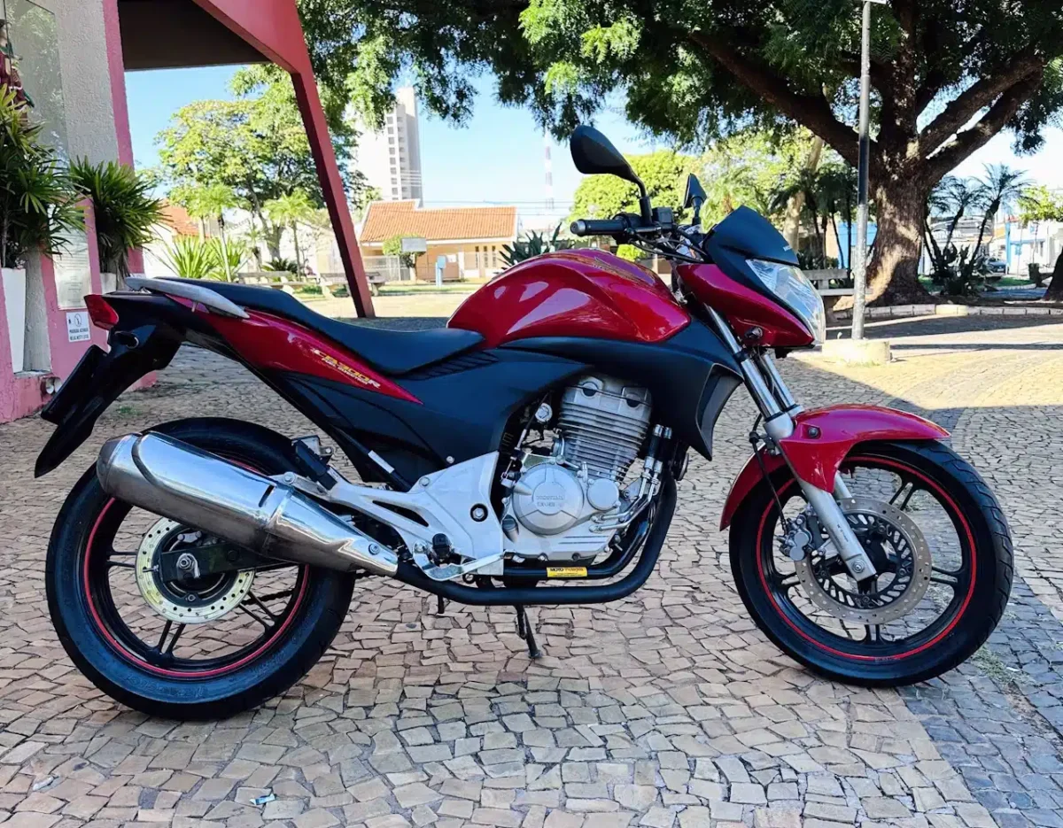 Red sport motorcycle parked on a patterned stone plaza with trees and buildings in the background.