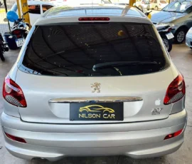 Rear of a silver Peugeot 207 in a car dealership lot, with a NILSON CAR plate and an Apple logo sticker on the right trunk.