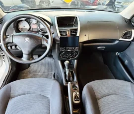 Interior of a car cockpit facing the driver: steering wheel, instrument cluster, center touchscreen, manual gear stick, and front seats visible.