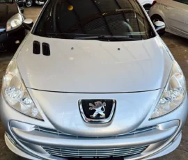 Front view of a silver Peugeot car in a showroom with its emblem visible on the grille and a Nilson Car plate.