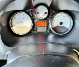 Dashboard instrument cluster with a left tachometer, right speedometer, and a central red digital display showing trip/odometer; steering wheel at bottom.