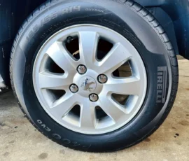 Silver alloy wheel with a black Pirelli tire (195/65 R14) mounted on a car, resting on a concrete surface.