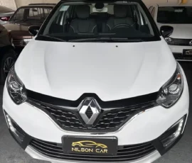 Front view of a white Renault SUV with prominent diamond logo, black grille, and headlights in a dealership setting (Nilson Car plate).