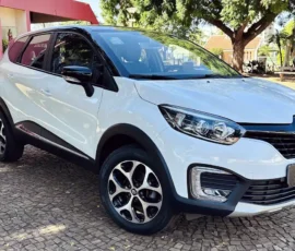Front three-quarter view of a white Renault SUV parked on a cobblestone surface with trees in the background.