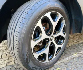 Close-up of a car wheel and tire mounted on a stylish alloy rim, on a cobblestone driveway edge near the wheel well.