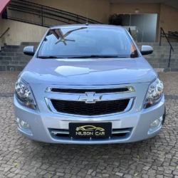 Vista frontal de um SUV Chevrolet prateado estacionado em uma área de paralelepípedos, com uma placa "Nilson Car" em primeiro plano.