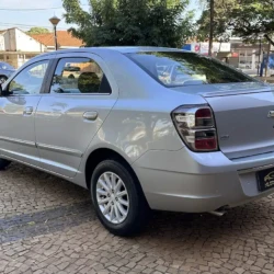 Sedã Chevrolet prateado estacionado em uma rua de paralelepípedos, visto de um ângulo de três quartos da traseira, exibindo o porta-malas e as lanternas traseiras.