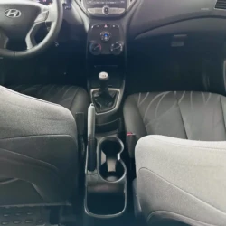 Front interior of a Hyundai car with steering wheel, central control panel, manual gear shift, and cup holders.