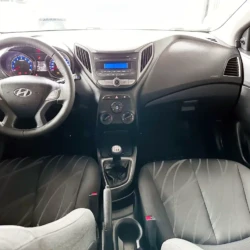 Front interior of a car showing the steering wheel, center console with radio, manual gear stick, and two front seats.