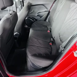Rear passenger seats of a compact car with black fabric upholstery and red seat belt buckles visible