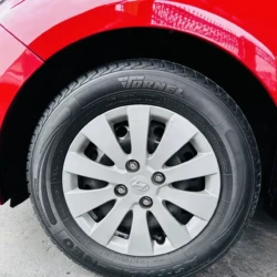 Close-up of a car tire and silver alloy wheel with Hyundai logo, under a bright red fender on a concrete surface.