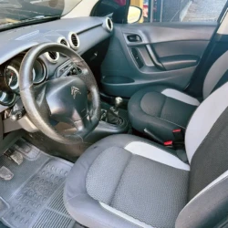 Front interior of a compact car with a manual gear shift, black and gray seats, and a three-spoke steering wheel.