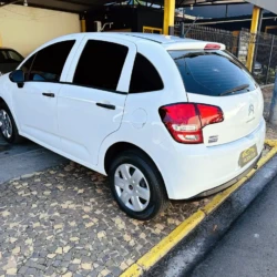 Rear three-quarter view of a white Citroën hatchback parked on a cobblestone driveway beside a yellow curb in a car lot.