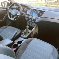 Interior of a modern car: steering wheel with VW logo, digital dashboard, center touchscreen, climate controls, and gear shifter visible between the front seats