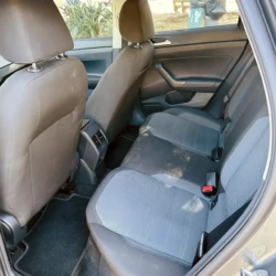 Interior of a car's rear seat area with two-tone fabric seats, headrests, and rear door panel visible. Seat belts are fastened; rear center console/vent area shown between front seats.